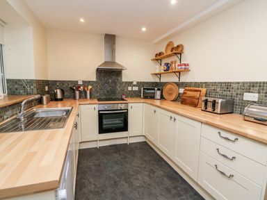 A kitchen with wooden countertops white cabinets a stainless steel sink oven toaster and shelves with kitchen items at Gwynfa Capel Iwan near Newcastle Emlyn