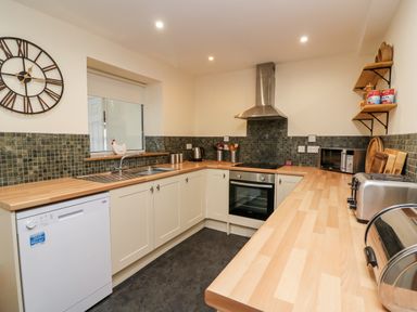 A kitchen with wooden countertops and cream cabinets a dishwasher an oven a toaster a microwave and shelves with canned goods at Gwynfa in Capel Iwan near Newcastle Emlyn