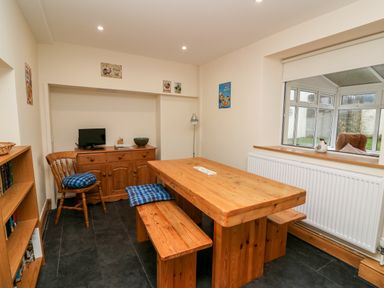 A dining room with a wooden table and benches and a wooden cabinet with a chair at Gwynfa in Capel Iwan near Newcastle Emlyn