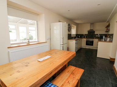 A kitchen with wooden dining table and benches a white refrigerator and built in oven with countertop at Gwynfa in Capel Iwan near Newcastle Emlyn