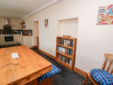 A kitchen with wooden table and chairs with blue cushions and a wooden bookshelf with books at Gwynfa in Capel Iwan near Newcastle Emlyn