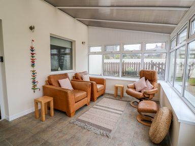 A sunroom with two brown armchairs a brown recliner with footrest two small wooden stools and a rug at Gwynfa Capel Iwan near Newcastle Emlyn