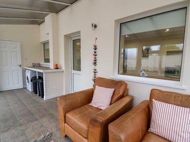 A room with two brown armchairs with striped cushions a washing machine bins a white door and a large window at Gwynfa in Capel Iwan near Newcastle Emlyn