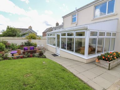 A glass conservatory attached to a house with a garden patio and seating area with purple cushions at Gwynfa in Capel Iwan near Newcastle Emlyn