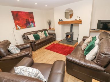 A living room with brown leather sofas a wood burning stove and a red rug at Gwynfa in Capel Iwan near Newcastle Emlyn