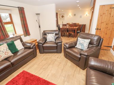 A living room with leather sofas and armchairs and a dining table in the background at Gwynfa in Capel Iwan near Newcastle Emlyn