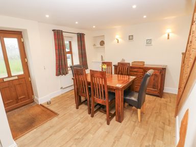 A dining room with a wooden table and chairs near a door and window at Gwynfa in Capel Iwan near Newcastle Emlyn