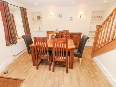 A dining area with wooden table and six chairs near a staircase and window with plaid curtains at Gwynfa Capel Iwan near Newcastle Emlyn
