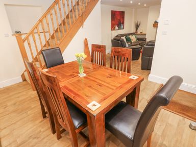 A dining area with wooden table and chairs next to a wooden staircase and a living room with leather sofas at Gwynfa in Capel Iwan near Newcastle Emlyn