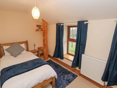 A bedroom with a single bed bedside table lamp window with curtains and a rug on the floor at Gwynfa in Capel Iwan near Newcastle Emlyn