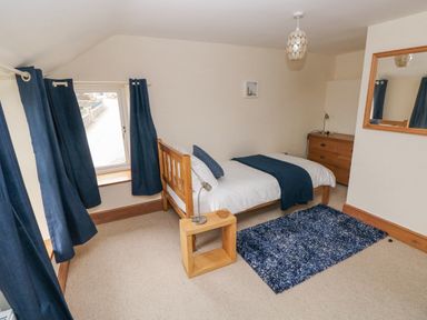 A bedroom with a single bed a wooden side table a dresser a window with blue curtains and a blue rug on the floor at Gwynfa in Capel Iwan near Newcastle Emlyn