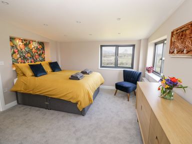 A bedroom with a double bed with yellow bedding and blue pillows a blue chair a wooden dresser with flowers and a carved wooden artwork on the wall at Phoenix House in Castlemorton