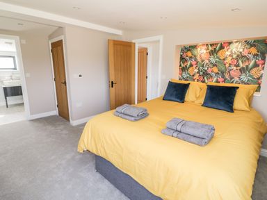 A bedroom with a yellow bedspread blue pillows folded towels and two wooden doors at Phoenix House in Castlemorton