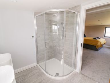 A bathroom with a glass shower enclosure and a view into a bedroom with a yellow bed at Phoenix House in Castlemorton