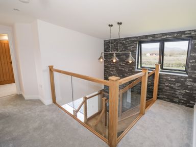 A carpeted upstairs hallway with glass and wood railing and a window with a view at Phoenix House in Castlemorton