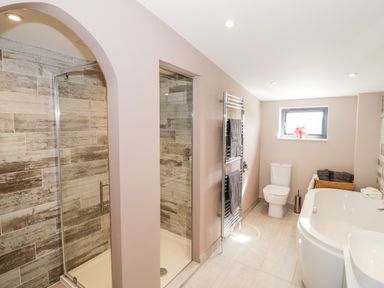 A bathroom with a shower, toilet, bathtub, towel rack, and a window at Phoenix House in Castlemorton