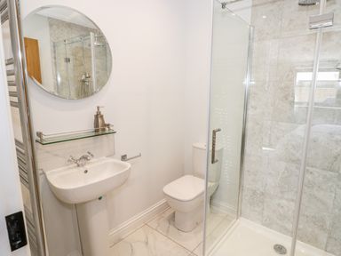 A bathroom with a pedestal sink a round mirror a toilet and a glass shower enclosure at Phoenix House in Castlemorton