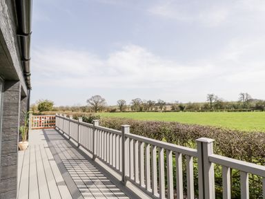 A balcony with a railing overlooking a green field and trees at Phoenix House in Castlemorton
