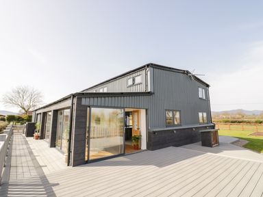An exterior view of a two story building with large windows and a spacious deck with plants on the deck at Phoenix House in Castlemorton