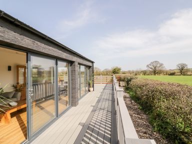 A deck with glass sliding doors opening to a living room and a view of fields at Phoenix House in Castlemorton