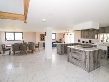 A kitchen and dining area with a wooden dining table and gray chairs next to a kitchen island with gray cabinets at Phoenix House in Castlemorton