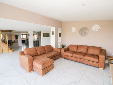 A living room with two brown sofas and decorative wall hangings at Phoenix House Castlemorton