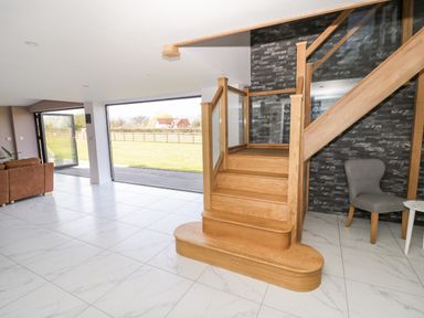 An open living space with wooden stairs gray chair and large windows showing a field at Phoenix House in Castlemorton