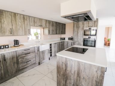 A kitchen with wood cabinets a white countertop an island with a cooktop a sink and built in ovens at Phoenix House in Castlemorton