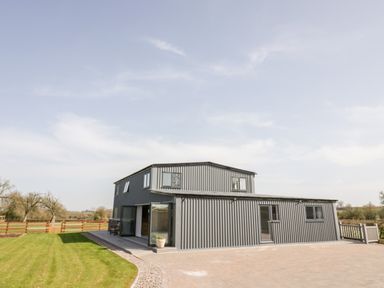 A two-story gray metal house with windows and doors surrounded by a green lawn and a wooden fence at Phoenix House in Castlemorton
