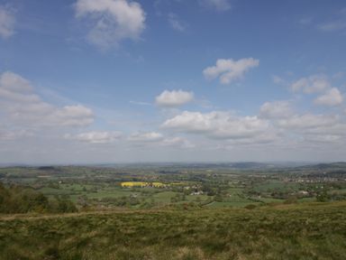 A rural landscape with green fields and scattered houses under a blue sky with clouds at Phoenix House in Castlemorton