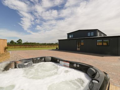 An outdoor hot tub on a paved patio in front of a black building with windows and a door at Phoenix House in Castlemorton
