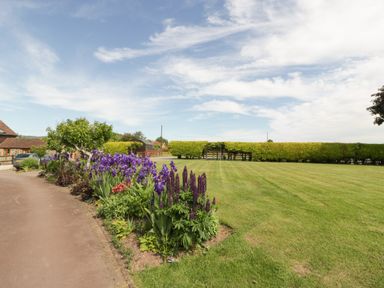 A garden with flower beds and a lawn bordered by hedges at Phoenix House in Castlemorton