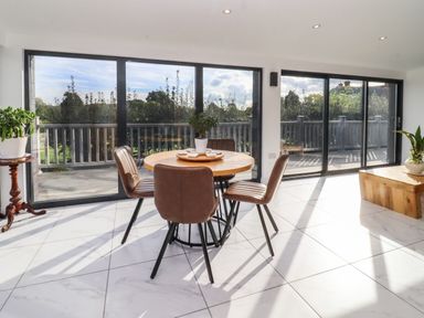 A dining area with round wooden table and four chairs next to large sliding glass doors with view of a fenced deck at Phoenix House in Castlemorton