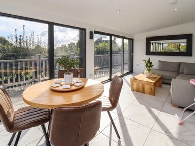 A dining area with round wooden table and chairs next to sliding glass doors and a living space with grey sofa and wooden coffee table at Phoenix House in Castlemorton