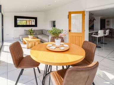 A dining area with a round wooden table and brown chairs near a living room with a gray sofa and wooden coffee table at Phoenix House in Castlemorton