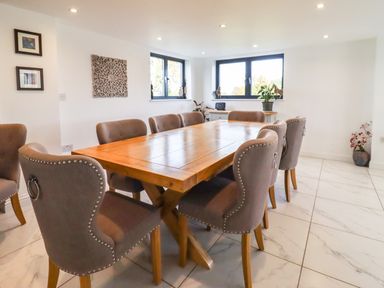 A dining room with a wooden table and upholstered chairs at Phoenix House in Castlemorton