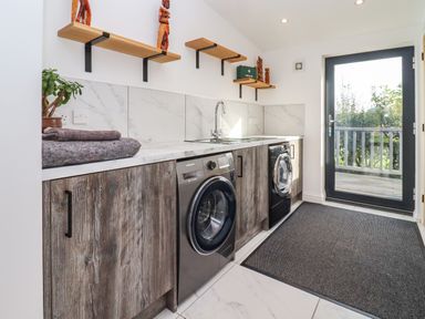 A laundry room with two washing machines wooden cabinets and shelves and a glass door at Phoenix House in Castlemorton