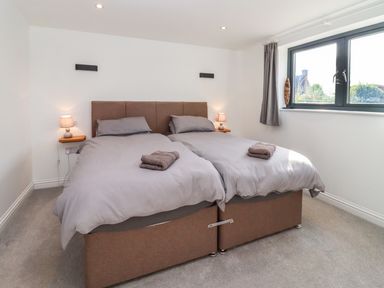 A bedroom with two single beds pushed together with gray bedding and towels on top at Phoenix House in Castlemorton