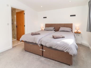 A bedroom with two single beds pushed together with gray bedding and towels on them at Phoenix House in Castlemorton