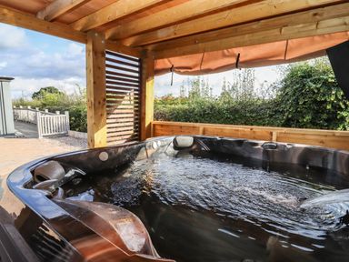 An outdoor hot tub under a wooden pergola with a privacy screen and greenery in the background at Phoenix House in Castlemorton