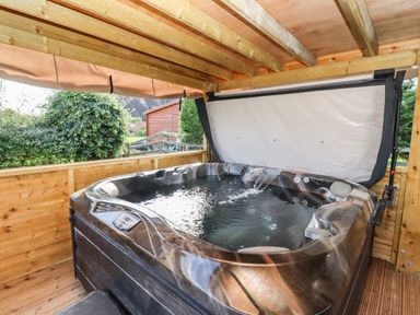 A covered outdoor hot tub with water jets and a garden shed in the background at Phoenix House in Castlemorton