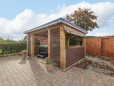 An outdoor wooden gazebo with a hot tub inside on a paved patio surrounded by plants at Phoenix House in Castlemorton