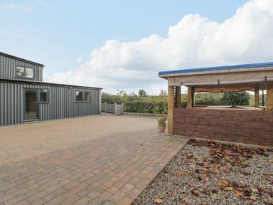 An outdoor paved area with a metal building and a wooden gazebo with a hot tub at Phoenix House in Castlemorton
