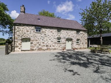 A stone house with two doors and five windows beside trees and picnic tables at Stabla in Chwilog