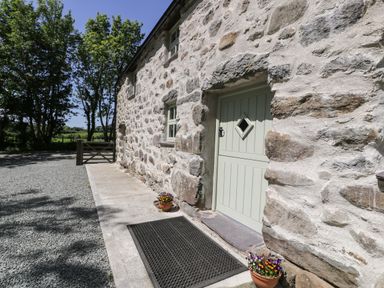 Stone exterior wall of a building with a green door and small windows next to a gravel pathway with flower pots at Stabla in Chwilog