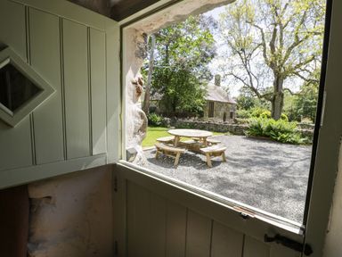 A green half door open to a gravel yard with a wooden picnic table and trees at Stabla in Chwilog