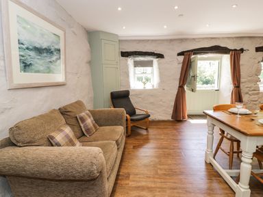 A room with a brown sofa with plaid cushions a black armchair and a wooden dining table with chairs at Stabla in Chwilog