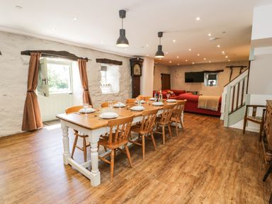A dining area with a wooden table set with plates and glasses alongside wooden chairs and a living area with red sofas and a wall-mounted TV at Stabla in Chwilog