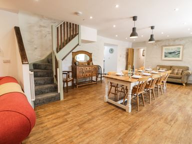 A dining table with chairs set for a meal near a staircase and a sofa in a room at Stabla in Chwilog