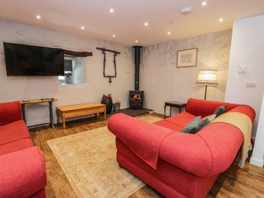 A living room with red sofas a television on the wall a wood burning stove and wooden tables at Stabla in Chwilog